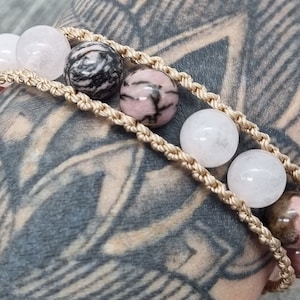 May include: A bracelet with pink, white, and black gemstone beads on a beige cord.