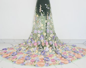 May include: Floral embroidered fabric in pastel colors. The fabric features a sheer, light green base with an array of embroidered flowers in shades of pink, purple, yellow, and peach. The flowers are densely arranged, creating a textured, three-dimensional effect.
