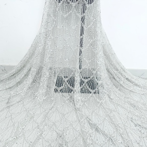 May include: White beaded fabric with a delicate, shimmering pattern. The fabric has a subtle sheen and a soft, flowing texture.