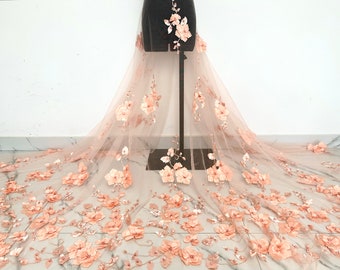 May include: Peach-colored tulle fabric with 3D floral appliques. The fabric is draped over a dress form and has a delicate, feminine look.