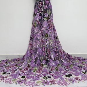 May include: Purple floral lace fabric with sequins. The fabric features a delicate mesh base with embroidered flowers and sequins in shades of purple, green, and pink.