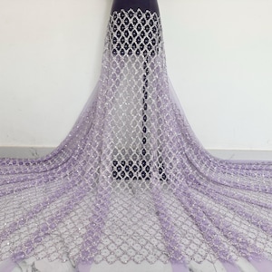 May include: A lilac and silver sequined fabric with a geometric pattern. The fabric is sheer and has a delicate texture.