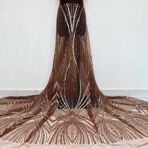 May include: A brown and gold sequined fabric with a geometric pattern. The fabric is sheer and has a delicate texture.