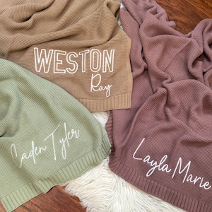 Pu&ograve; includere: Tre coperte lavorate a maglia nei colori marrone chiaro, verde salvia e malva. La coperta marrone chiaro presenta il testo bianco 'WESTON Ray', quella verde salvia il testo 'Caden Tyler' e quella malva il testo 'Layla Marie'.