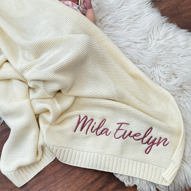Pu&ograve; includere: Una coperta per neonati lavorata a maglia color crema con un motivo a punto legaccio testurizzato e un bordo a coste. Il nome Mila Evelyn &egrave; ricamato in un carattere corsivo color malva scuro sulla parte inferiore del tessuto, creando un look personalizzato.