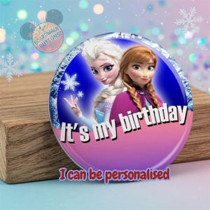 May include: A round button featuring Elsa and Anna from Frozen, with the text "It's my birthday" in white. The button has a blue and pink background and the text "I can be personalised" in red.