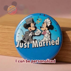 May include: A blue circular button with Mickey and Minnie Mouse dressed for a wedding, with the words "Just Married" in white. The button has a light blue background with confetti and the text "I can be personalised".