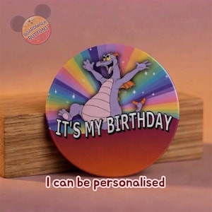 Puede incluir: Un botón redondo con un personaje de dragón de dibujos animados en el centro, sobre un fondo de arcoíris. El texto "IT'S MY BIRTHDAY" se muestra en blanco. El botón tiene el texto "I can be personalised" en la parte inferior.