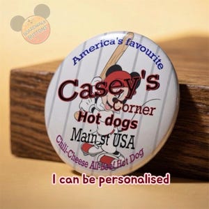 May include: A round button with the text "America's favourite Casey's Corner Hot dogs Main st USA Chili-Cheese All-Beef Hot Dog". The button features a cartoon character holding a baseball bat. The text "I can be personalised" is also on the button.