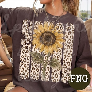 Op de afbeelding: Een donkerbruin t-shirt met korte mouwen en een grote grafische print van een gele zonnebloem, gecentreerd over verticale strepen met een beige en bruin luipaardpatroon. Het ontwerp heeft een verweerde, getextureerde uitstraling.