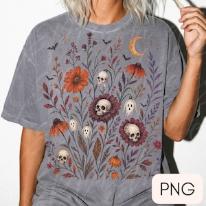 K&ouml;nnte beinhalten: Ein anthrazitfarbenes Kurzarm-T-Shirt mit einem Grafikdruck aus orangefarbenen und violetten Wildblumen, menschlichen Sch&auml;deln, kleinen Geisterfiguren und Flederm&auml;usen. Oben rechts befindet sich eine Mondsichel im botanischen Design.
