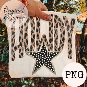 May include: A white t-shirt featuring the word HOWDY in a tan and black leopard print pattern. Below the text is a large five-pointed star with a black background, white polka dots, and a gold-colored outline. The design is centered.