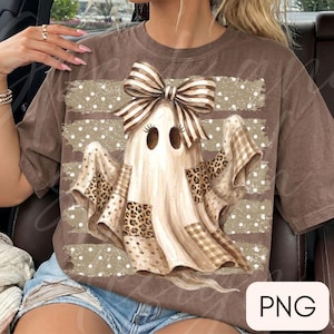 Może przedstawiać: Brązowy t-shirt z grafiką ducha z długimi rzęsami i dużą, pasiastą kokardą na głowie. Duch jest ozdobiony łatami w panterkę i brązową kratę, umieszczony na tle w białe kropki ułożone w poziome pasy na całej powierzchni nadruku.