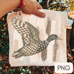 May include: A light-colored fabric item featuring a graphic of a flying duck. The duck's body is decorated with a mix of patterns including a black and white checkerboard, leopard print, and polka dots, set against a background of vertical brushstrokes.