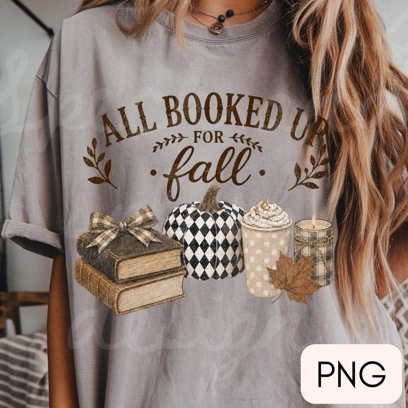 May include: A grey t-shirt featuring the brown text ALL BOOKED UP FOR fall, accompanied by a stack of two books with a plaid bow, a black and white checkered pumpkin, a cup of coffee with whipped cream, a lit candle, and a brown leaf.