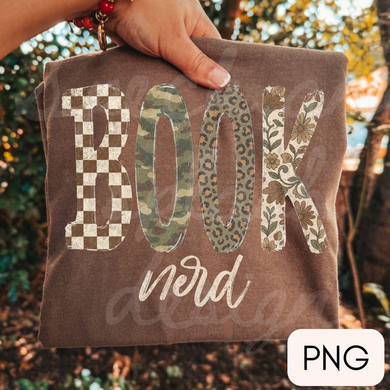 Op de afbeelding: Een bruin t-shirt met het woord BOOK in grote blokletters, elk met een ander patroon: bruin en wit dambord, groen camouflage, luipaardprint en een bloemmotief. Het woord nerd staat eronder gedrukt in wit cursief schrift.