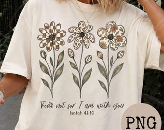 May include: A cream-colored t-shirt featuring a graphic of three flowers with stems and leaves. The flower petals have different patterns including a brown and white checkerboard, leopard print, and floral print. The text reads Fear not for I am with you Isaiah 41:10.