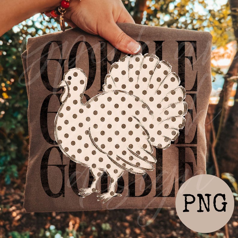 May include: A brown t-shirt featuring a large white turkey graphic covered in dark brown polka dots. The background of the design displays the word GOBBLE repeated three times in a bold, dark brown, distressed sans-serif font.