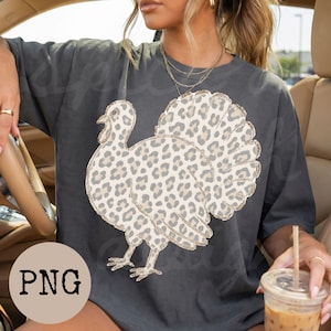 May include: A charcoal gray short-sleeve t-shirt featuring a large graphic of a turkey with a beige and brown leopard print pattern. The turkey is depicted in profile, showcasing its fanned-out tail feathers and detailed plumage with a spotted design.