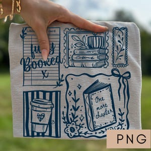 May include: A light beige t-shirt with a dark blue graphic design featuring book-themed illustrations. The design includes a coffee cup, a library card, a stack of books, and the text "fully booked" and "One more chapter".