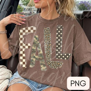 May include: A brown short-sleeve t-shirt featuring the word FALL printed in large letters. Each letter has a distinct pattern: the F is a brown and white checkerboard, the A is camouflage, the L is leopard print, and the L is black with white dots.