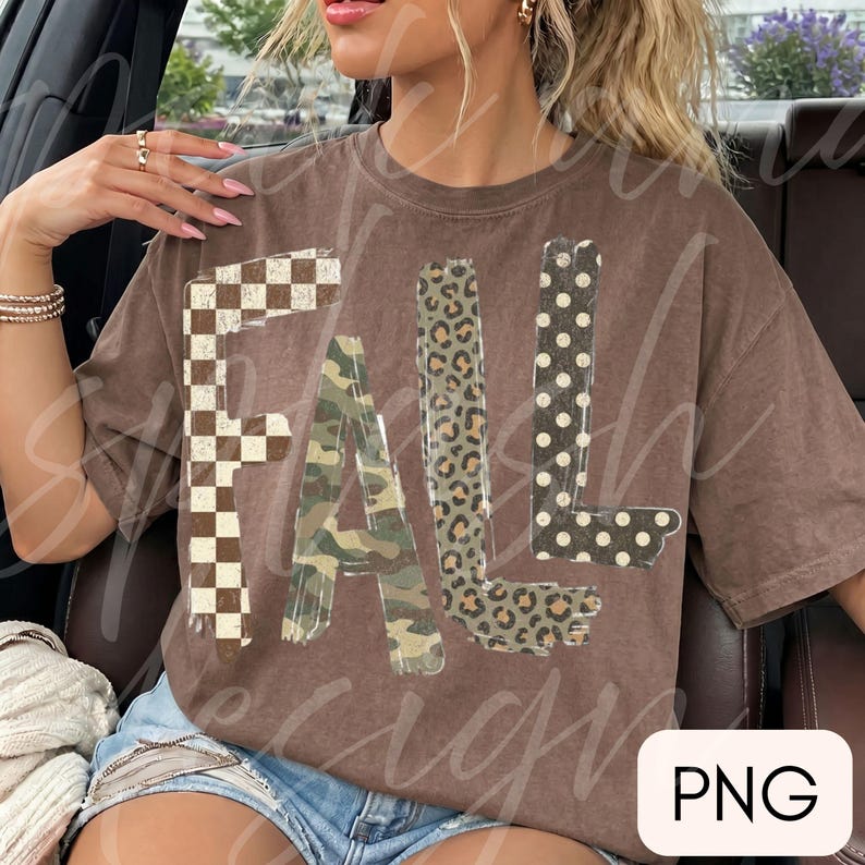 May include: A brown short-sleeve t-shirt featuring the word FALL printed in large letters. Each letter has a distinct pattern: the F is a brown and white checkerboard, the A is camouflage, the L is leopard print, and the L is black with white dots.