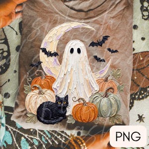 May include: A brown t-shirt featuring a textured, impasto-style graphic of a white ghost standing before a crescent moon. The design includes a black cat, several pumpkins in shades of orange and sage green, and small black bats flying overhead.