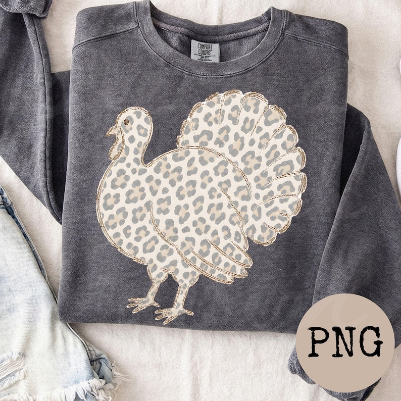 May include: A charcoal gray crewneck sweatshirt featuring a graphic of a turkey with a beige and brown leopard print pattern. The turkey design has a thin gold outline. The garment has a label at the inner neckline that reads Comfort Colors.