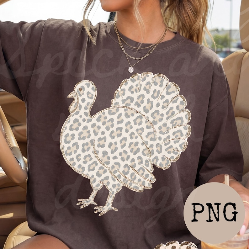 May include: A dark brown short-sleeve t-shirt featuring a large graphic of a turkey with a beige and grey leopard print pattern. The turkey graphic has a thin gold outline. The shirt has a crew neckline and a relaxed, loose-fitting silhouette.