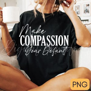May include: Black t-shirt with the white text "Make COMPASSION Your Default." A person is holding a white mug. The shirt is a dark color and the text is in a handwritten style font.