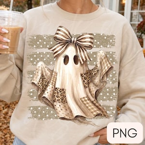 Könnte beinhalten: Ein beigefarbenes Sweatshirt mit Rundhalsausschnitt und einem zentralen Grafikdruck eines Geistes mit einer großen gestreiften Schleife. Der Geist hat Leopardenmuster- und Karomuster-Einsätze auf einem Hintergrund aus horizontalen Pinselstrichen.