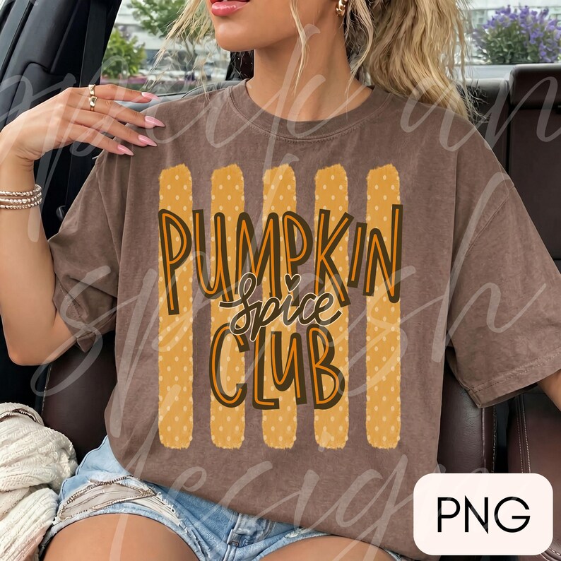 May include: A brown short-sleeved t-shirt featuring a graphic design of five vertical yellow stripes with white polka dots. The text PUMPKIN SPICE CLUB is printed in a dark brown and orange font over the stripes, with a small heart above the word spice.