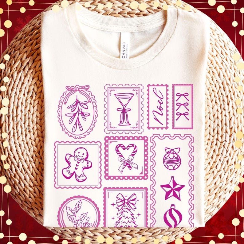 May include: Cream-colored t-shirt featuring a collection of pink Christmas-themed postage stamp designs. The stamps include images of a gingerbread man, ornaments, bows, and the word "Noel". The shirt is made of a soft material.