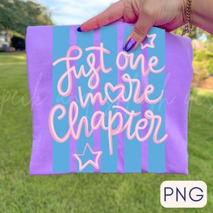May include: A lilac-colored t-shirt with a light blue striped design. The shirt features the text "Just one more chapter" in pink script, with star and heart accents. The shirt is held up by a person.
