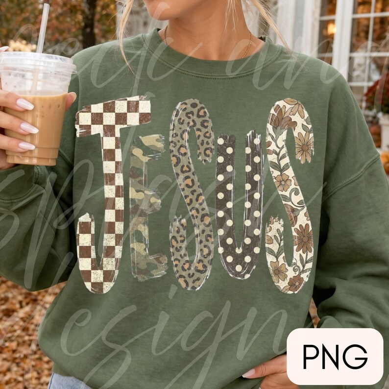 May include: An olive green crewneck sweatshirt featuring the word JESUS in large, stylized letters. Each letter has a unique pattern: a brown and white checkerboard, camouflage, leopard print, white polka dots, and a brown floral print.