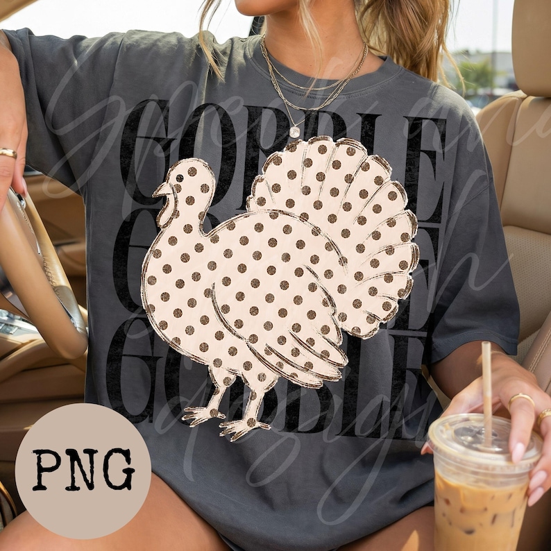 May include: A charcoal gray short-sleeve t-shirt featuring a large graphic of a turkey with a tan body and brown polka dots. The background text reads GOBBLE in a distressed black font. The shirt has a crew neckline and a relaxed fit design.