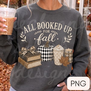 May include: A charcoal gray crewneck sweatshirt featuring a graphic print with the text ALL BOOKED UP FOR fall. The design includes a stack of two books with a plaid bow, a black and white checkered pumpkin, a coffee cup, and a plaid candle.
