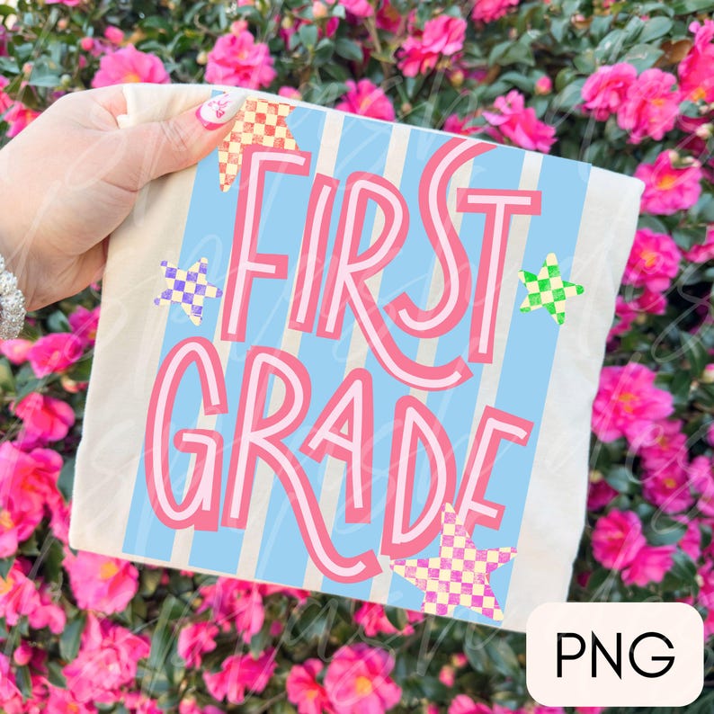 May include: A white t-shirt featuring a light blue and white vertical striped rectangular graphic with the pink text FIRST GRADE. The design includes three checkered stars in yellow, purple, and green, positioned around the bold pink lettering.