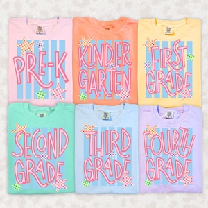 May include: Six t-shirts in pastel colours featuring vertical light blue stripes and pink text reading Pre-K, Kindergarten, First Grade, Second Grade, Third Grade, and Fourth Grade. Each shirt is decorated with small, colourful checkered stars.