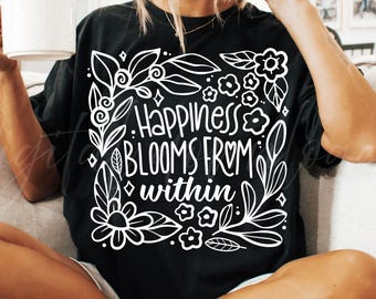 Pode incluir: Camiseta preta com um design floral branco e as palavras "Happiness Blooms From Within". O design inclui flores, folhas e elementos decorativos. O texto "SVG & PNG" aparece na parte inferior.