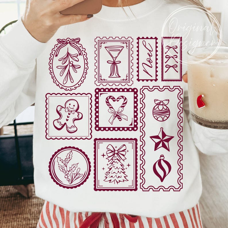 May include: White sweatshirt with a festive design featuring various Christmas-themed illustrations in a deep red color. The design includes a gingerbread man, candy canes, a Christmas tree, and the word "Noel".