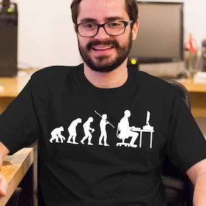 Peut inclure: Un t-shirt noir avec un graphique blanc représentant l'évolution de l'homme, se terminant par une personne assise devant un ordinateur. Le graphique représente la progression d'un singe primitif à un humain moderne utilisant un ordinateur.