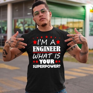 Könnte beinhalten: Schwarzes T-Shirt mit weißem Text, der "I'm a Engineer What is Your Superpower?" lautet, mit roten Sternen um den Text herum.