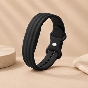 Può includere: Un cinturino per orologio in silicone nero opaco caratterizzato da un design liscio e flessibile con tre distinte creste orizzontali lungo la fascia. Il cinturino include una chiusura con perno in metallo e fori per la regolazione.