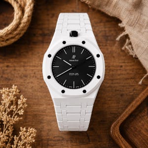 May include: A white wristwatch with a black circular dial featuring the text AP Audemars Piguet and Royal Oak Pocket Watch. The watch has a white link bracelet, a white octagonal bezel with black hexagonal screws, and a black crown at the top.