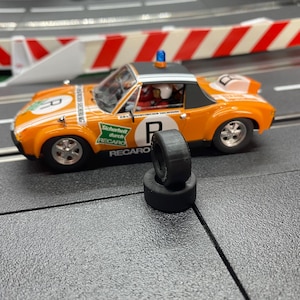 Könnte beinhalten: Orangenes und weißes Spielzeug-Rennauto mit schwarzen Reifen. Das Auto hat die Nummer "8" und das Wort "RECARO" aufgedruckt. Ein Paar schwarze Reifen befinden sich vor dem Auto.