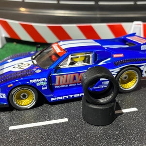 May include: A blue and white race car model with the number 32, gold wheels, and black tires. The car has sponsor logos and is on a track with red and white barriers.