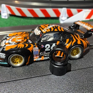 May include: A black and orange toy race car with a tiger stripe design. The car has the number 24 on the side and the word "Super" on the back. The car is on a black track with white lines. There are four black tires next to the car.