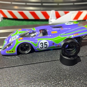 May include: A purple and green toy race car with the number 35 on the side. The car is on a black track with a red and white barrier in the background. The car has a black tire and a black rim.