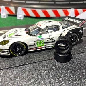 May include: A white and black race car with the number 72 on the side. The car has a Dunlop spoiler and is on a black track. There are three black tires stacked on the track.